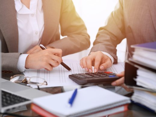 Two female accountants counting on calculator income for tax form completion hands close-up. Business and audit concept Two female accountants counting on calculator income for tax form completion hands close-up. Business and audit concept